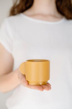 A serene close-up shot of a woman holding a yellow mug, offering simplicity and warmth.