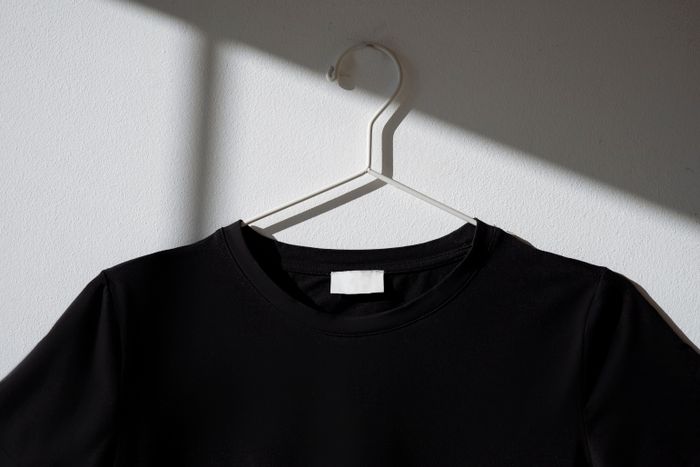 A plain black shirt on a wire hanger against a bare wall, photo by Hanna Pad on Pexels