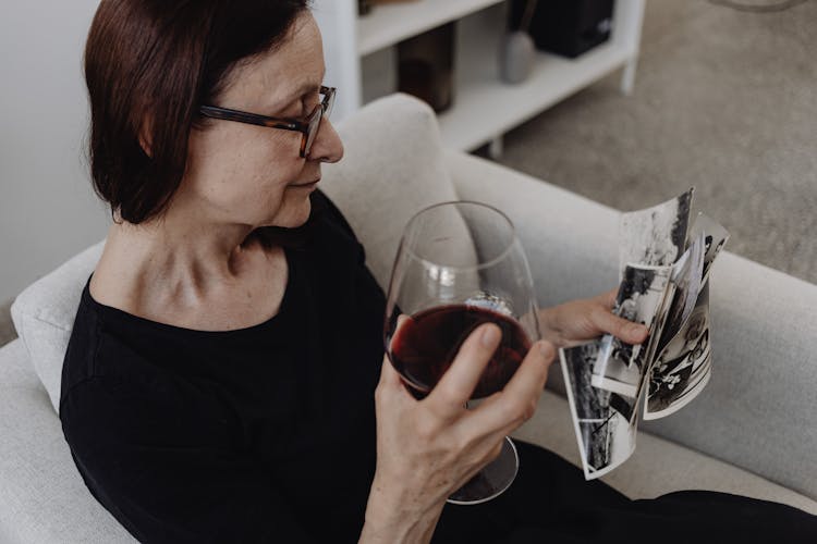 A Woman In Black Dress Holding A Glass Of Red Wine And A Bunch Of Old Photos