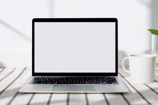 A minimalist home office setup with a blank-screen laptop and mug, bathed in natural light.