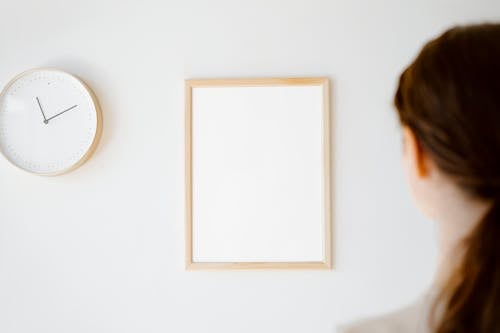 Free Woman Looking at Blank Picture Frame and Clock on the Wall Stock Photo