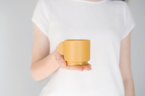 Free Minimalist photo of an adult holding a mustard yellow cup. Stock Photo