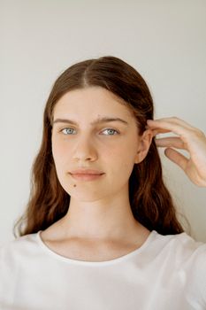 Close-up portrait of a woman with long brown hair and a natural expression against a neutral background.
