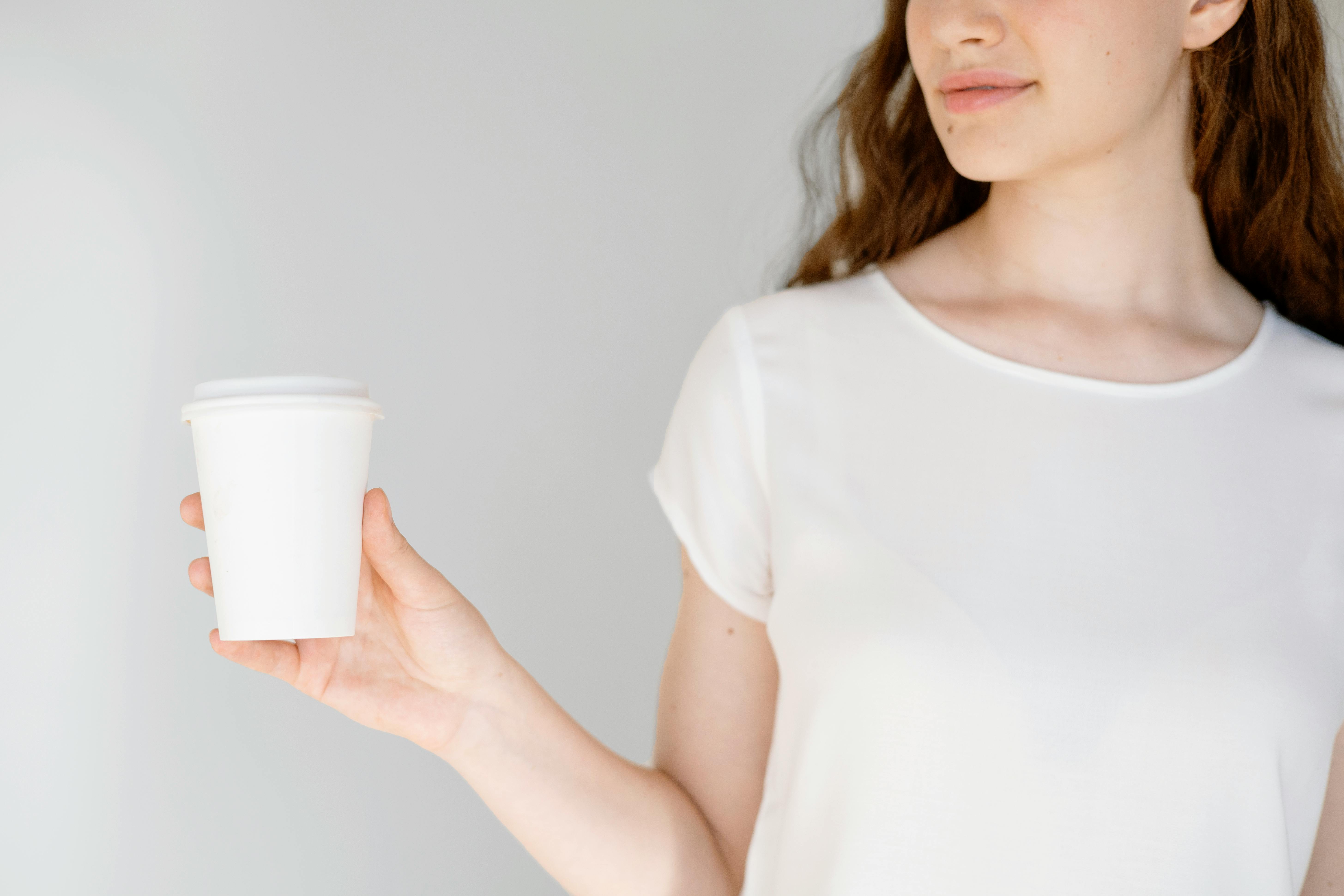 A woman in a white blouse holding a disposable coffee cup. Minimalist indoor portrait.