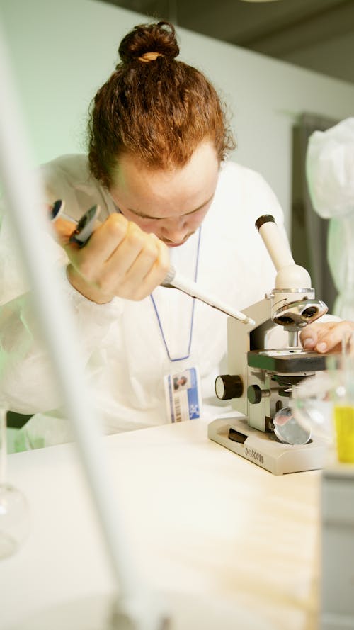 A Man in White T-shirt Holding a Lab Equipment Near a Microscope