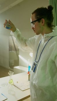 Scientist in lab coat analyzing blue liquid in laboratory setting.