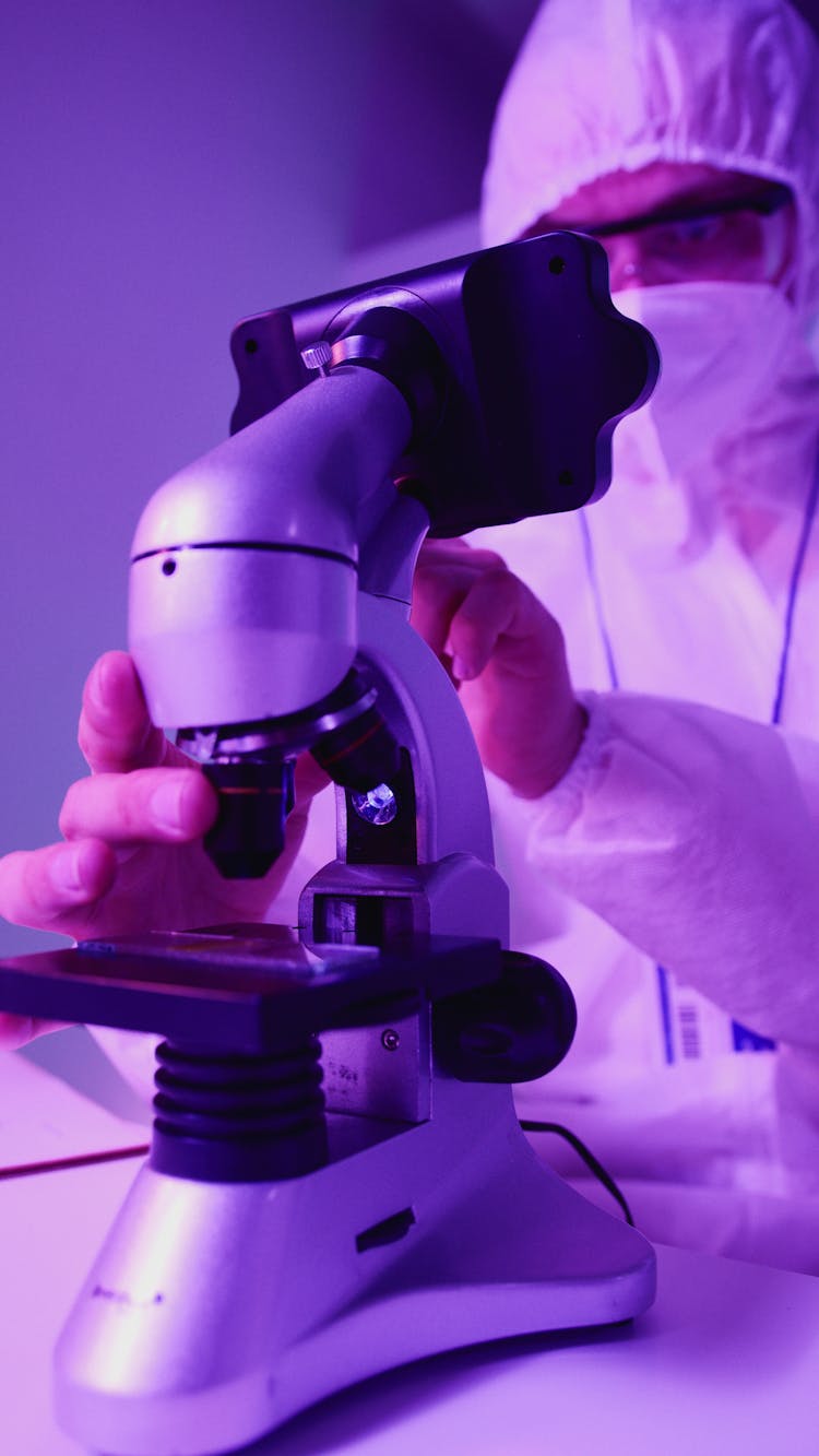 Scientist In Personal Protective Equipment Using A Microscope