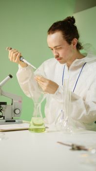 Young scientist using a pipette in a lab, focusing on research with a microscope.