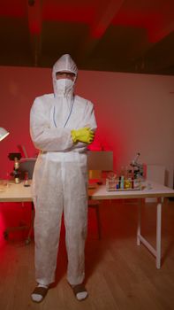 Scientist in protective gear standing in laboratory with red lighting.