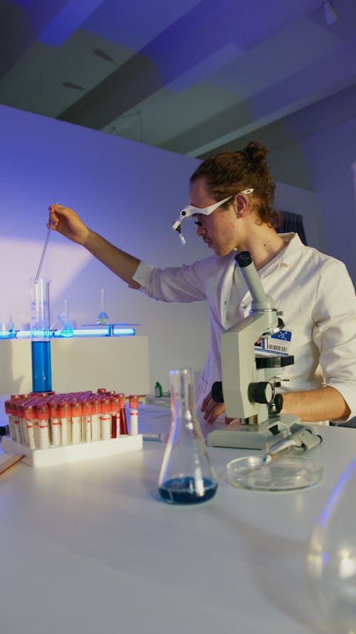 A Man Wearing a Magnifying Eyewear Holding a Pipette in a Graduated Cylinder