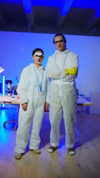 Two scientists in full PPE stand in a blue-lit laboratory environment.