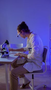 A scientist in a lab coat examines data while using a microscope in a modern laboratory setting.