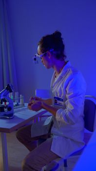 Scientist working with microscope and test tubes in a laboratory with blue lighting.