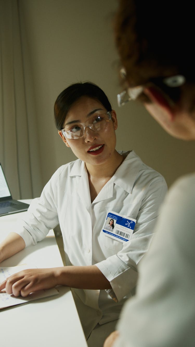 A Woman In White Button Up Shirt Wearing Medical Goggles With ID Pinned On Shirt