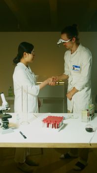 Two chemists shaking hands in a well-equipped laboratory, showcasing teamwork and collaboration.