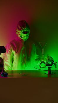 A scientist in full protective gear experiments with glowing chemicals in a dark lab.