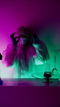 A scientist in protective gear performing an experiment with colorful flasks in a lab.