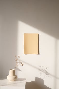 Elegant minimalist interior with ceramic vase and paper against a sunny wall.