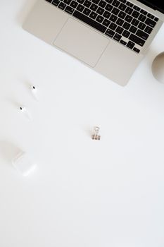 Clean minimalist workspace featuring a laptop, wireless earphones, and a white background, perfect for productivity.