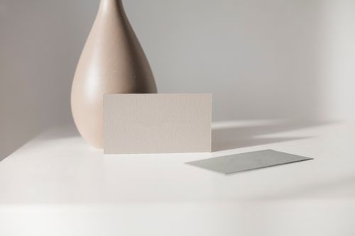 Free Elegant minimalist mockup featuring a blank card and ceramic vase on a white table. Perfect for branding or design. Stock Photo