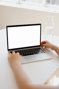 A clean, modern workspace featuring a laptop with a blank screen and a pitcher of water.