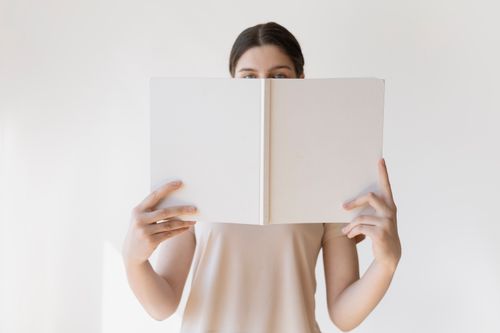 Free A young woman holds a blank book in front of her face, ideal for mockup purposes. Stock Photo