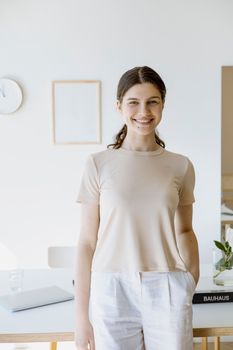 A young woman smiling indoors in a minimalist room, emitting a warm and inviting vibe.