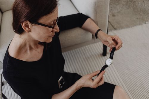Free A woman sits indoors, pensively holding a wristwatch, conveying contemplation. Stock Photo