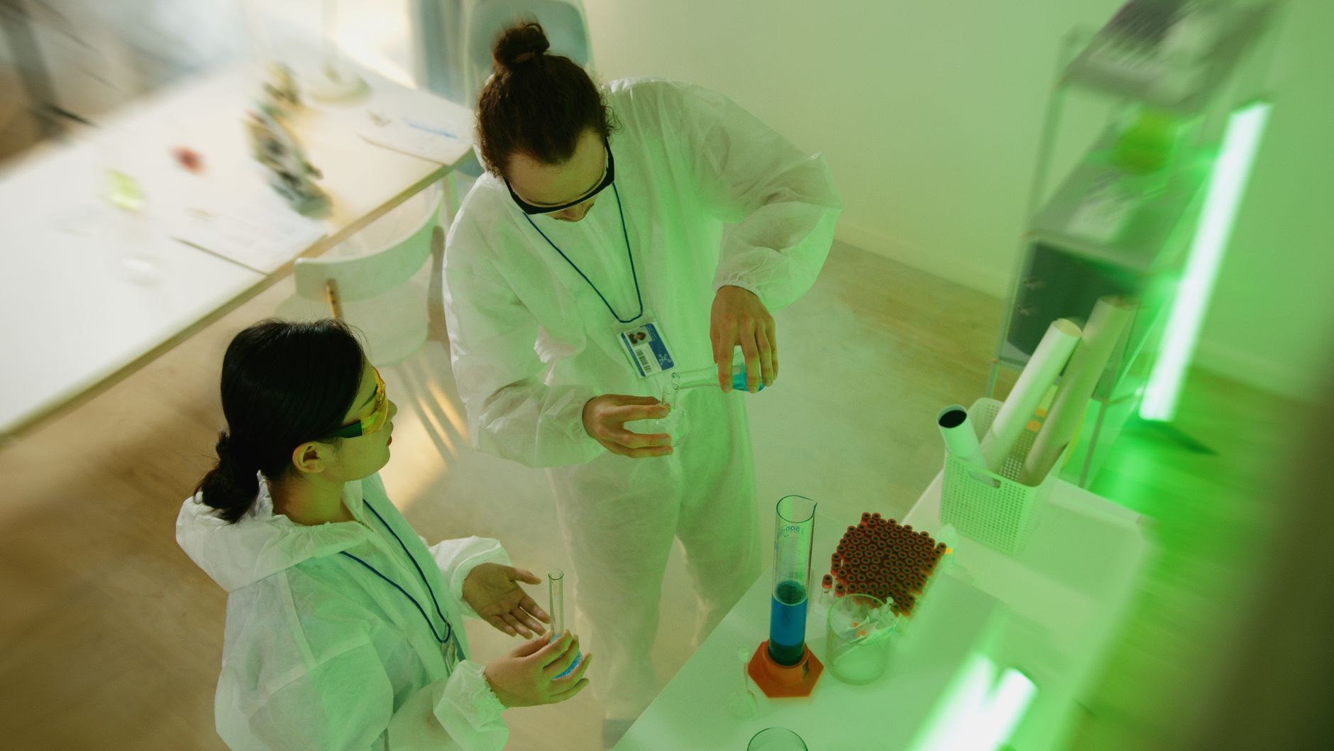 Two scientists in protective clothing conducting a laboratory experiment with beakers.