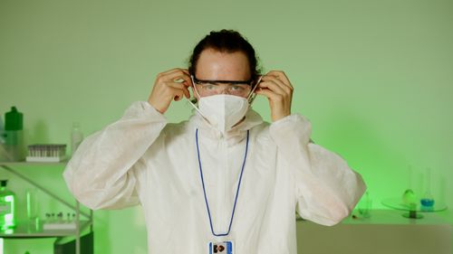 Free Scientist wearing protective gear in a laboratory with green lighting. Stock Photo