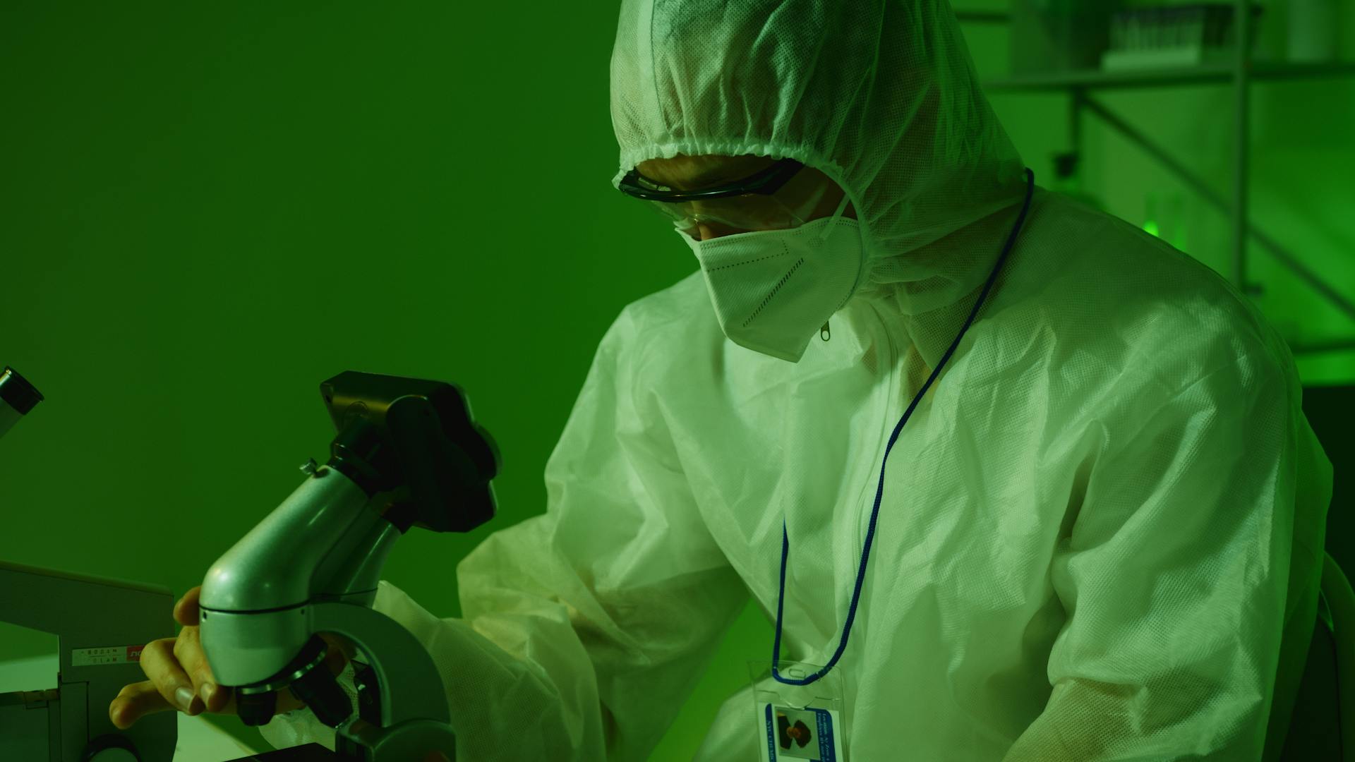 Person in Personal Protective Equipment Holding a Microscope