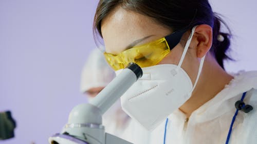 Free A Person Wearing Personal Protective Equipment Looking Through a Microscope Stock Photo