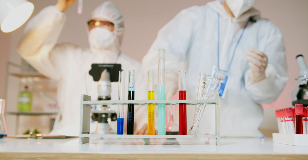Two scientists with protective gear working with test tubes in a modern lab setup.