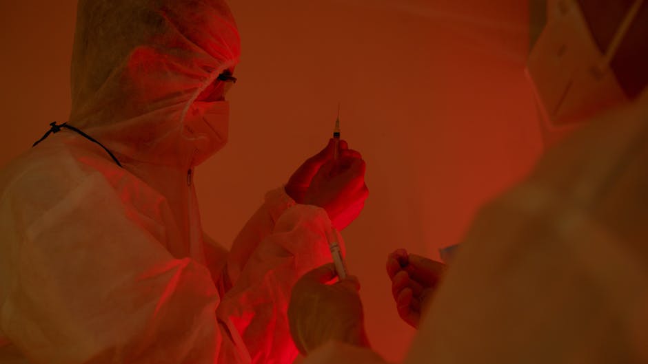 Researchers in protective suits and masks preparing syringes in a laboratory setting.