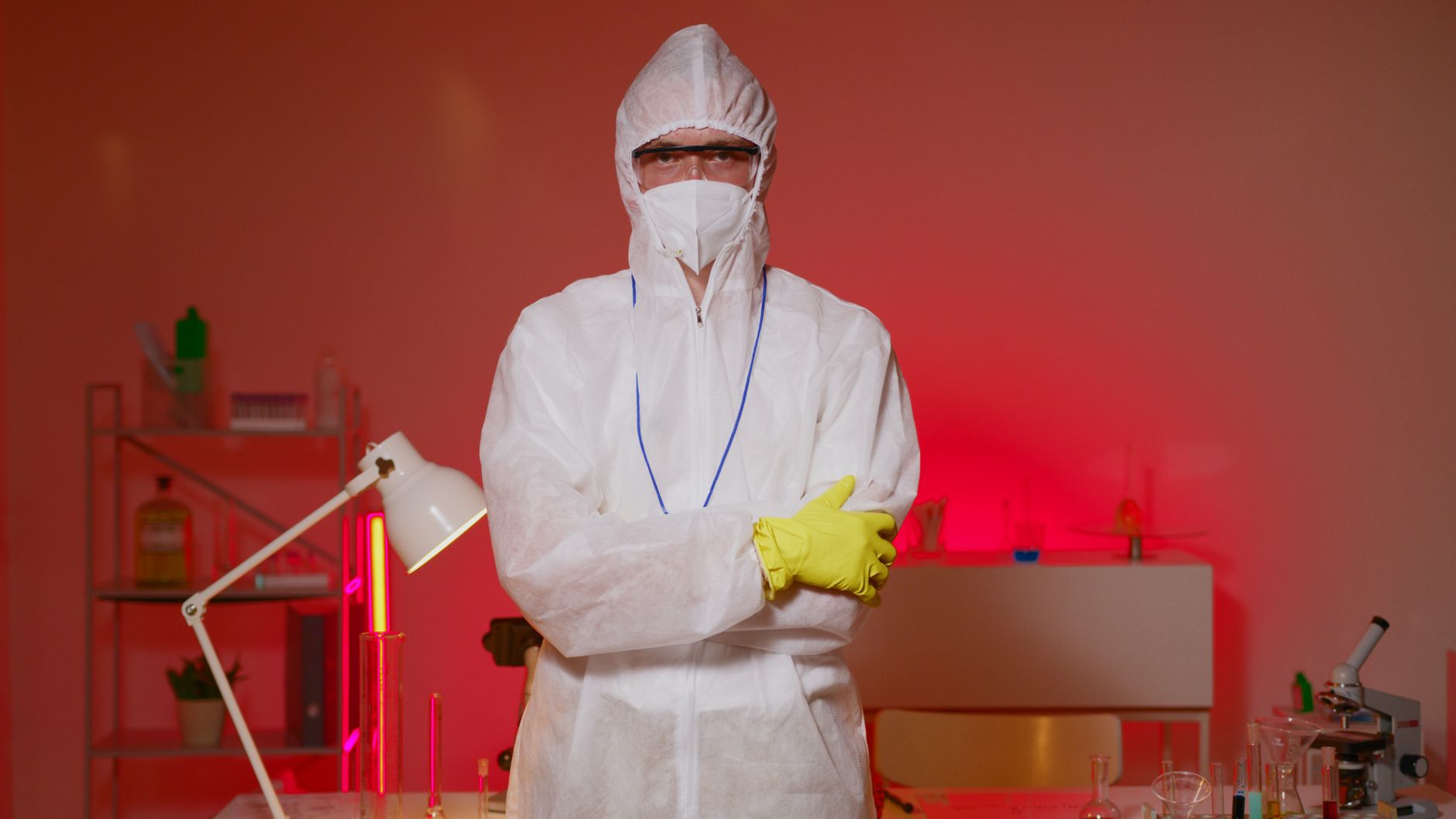 Fachkraft in weißem Schutzanzug mit Maske und gelben Handschuhen in einem Labor.