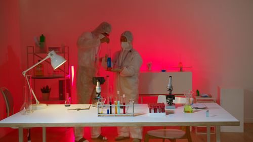 Free Scientists in a lab analyzing chemical substances under colored lighting, focusing on safety and innovation. Stock Photo