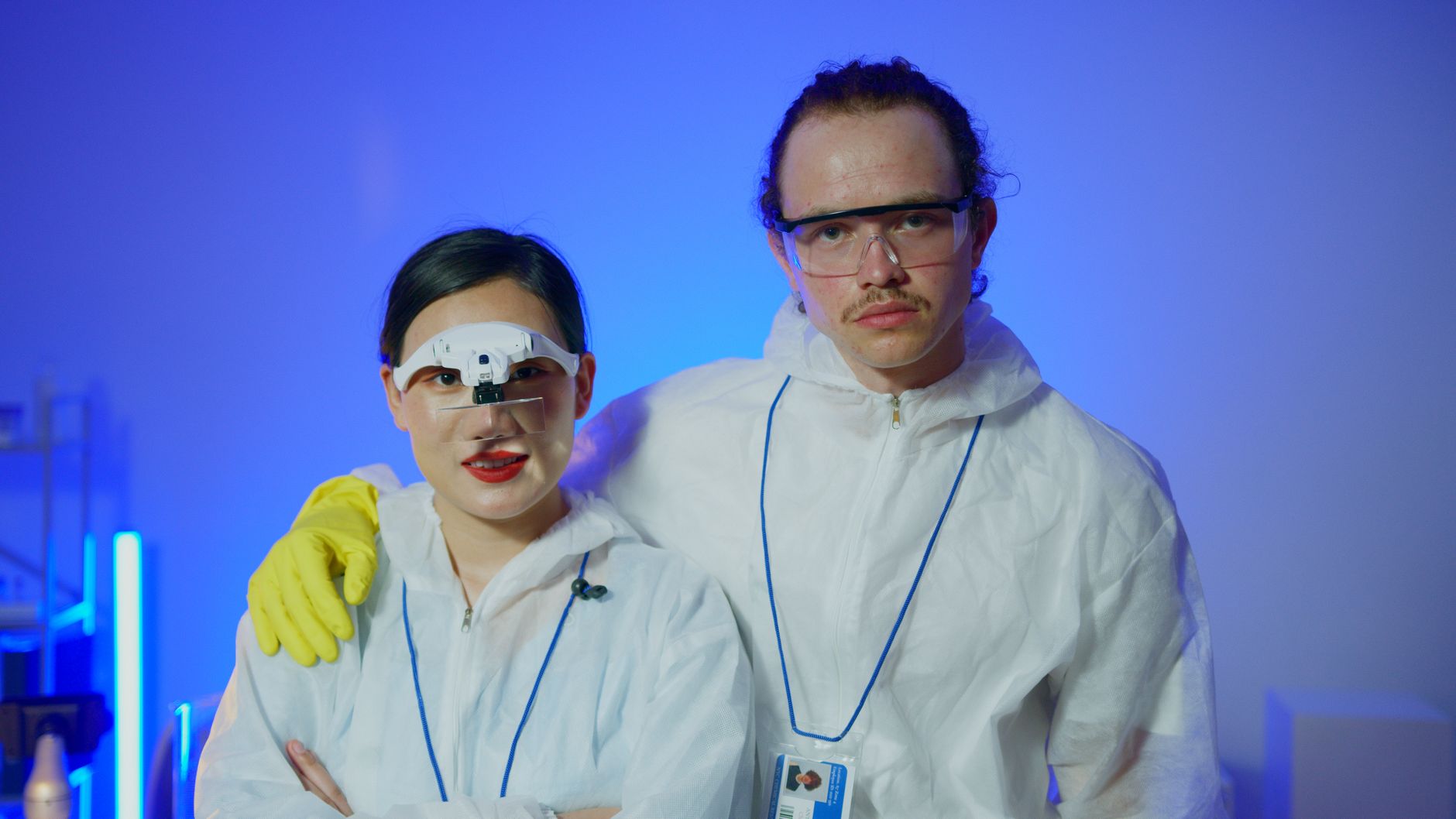 Two scientists in protective gear posing in a lab with safety goggles and lab coats.