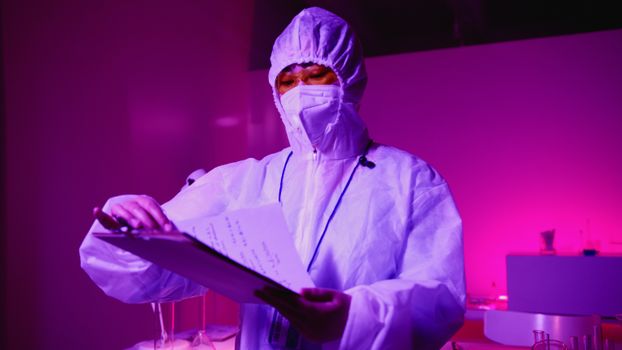A scientist in protective gear examines notes in a vibrant laboratory setting.