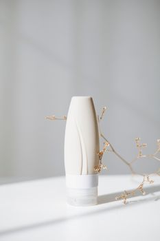 Elegant skincare cream bottle with a natural branch in soft lighting.