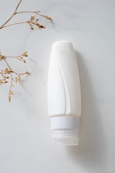 Minimalist white cosmetic bottle placed on a white surface next to dried plant stems.