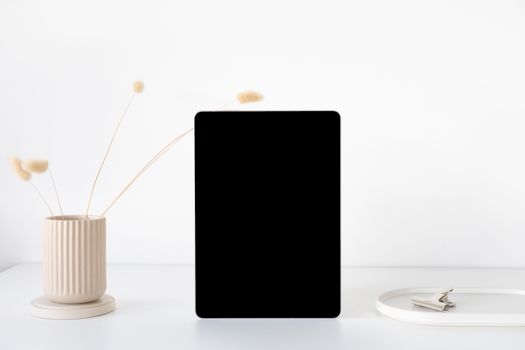 A minimalist mockup of an iPad on a white desk with a neutral vase and accessories, perfect for showcasing digital content.