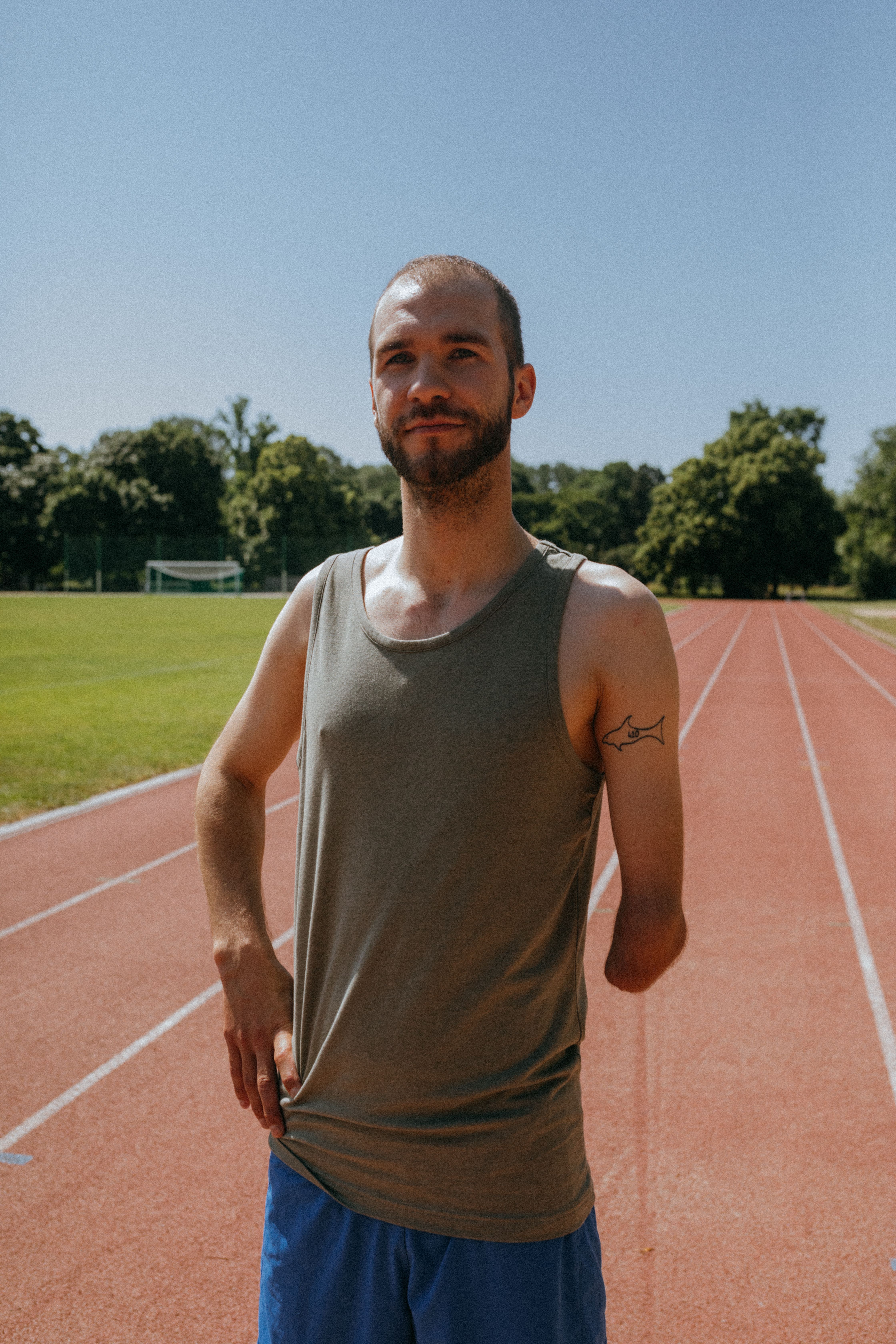 A confident man with a prosthetic arm standing on an outdoor running track in sunlight.
