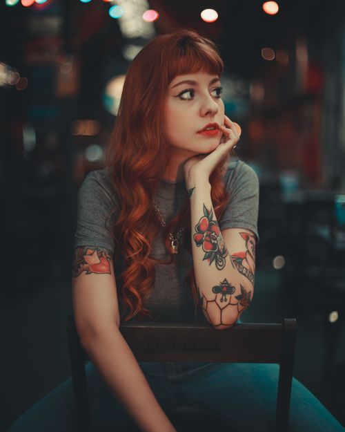 Free Young woman with tattoos gazes thoughtfully in dimly lit urban café. Stock Photo