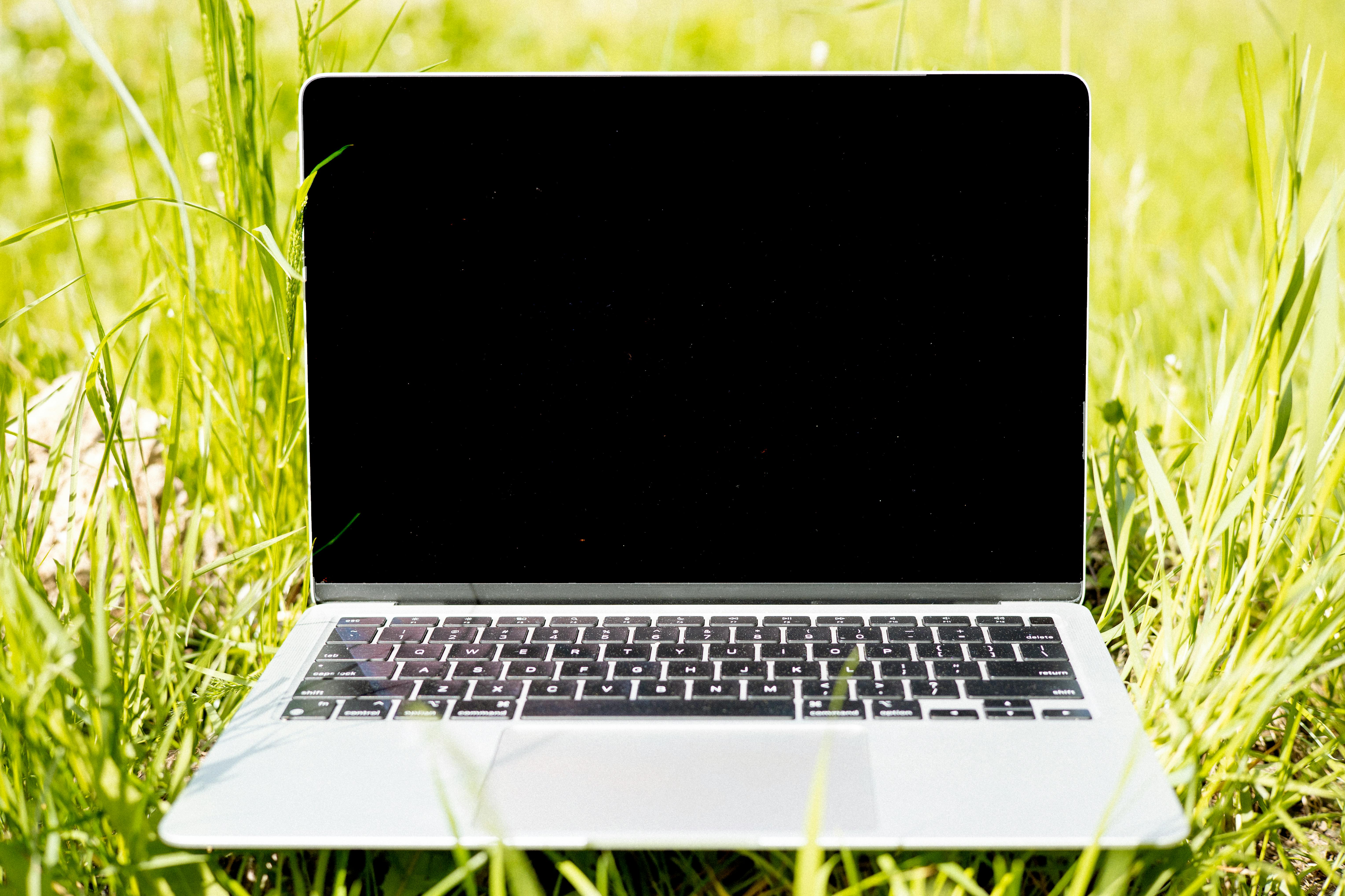Laptop on green grass in sunlight. Ideal for remote work and technology themes.
