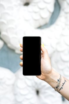A hand with tattoos and bracelets holding a black smartphone, ideal for showcasing digital devices.