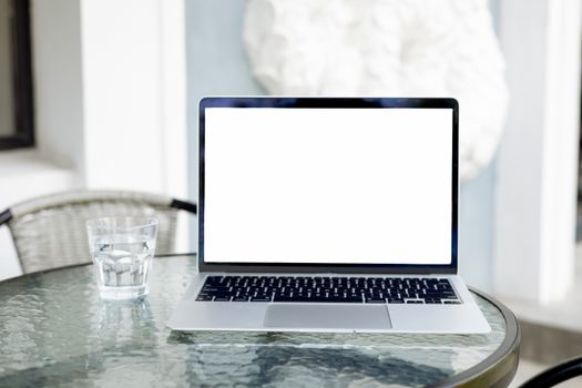 Image of an open laptop with a blank screen on a glass table, next to a glass of water.