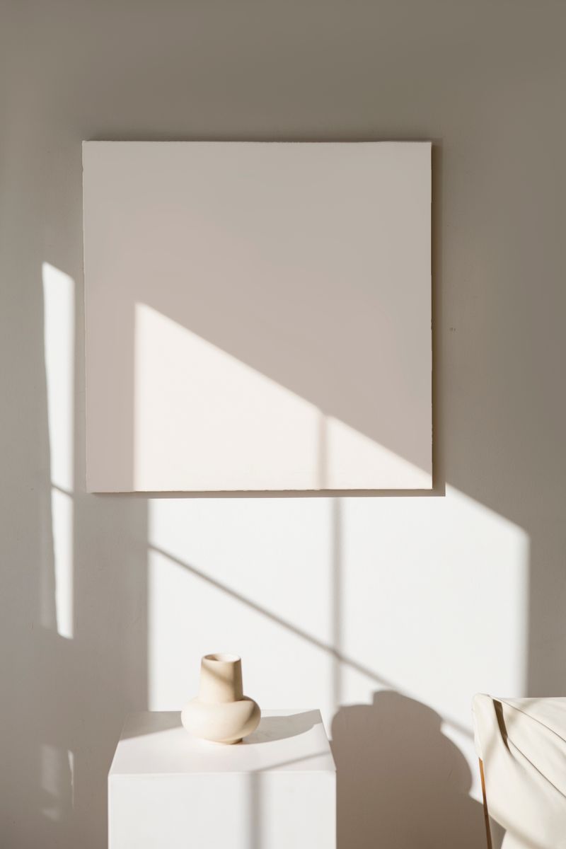 A serene minimalist art exhibit featuring an empty canvas and simple pottery.