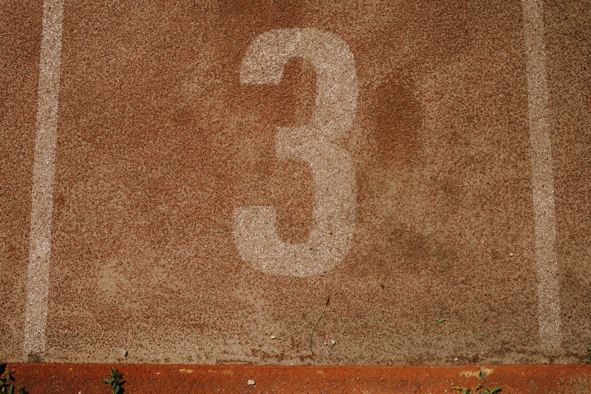 Close-up of a textured running track with the number three, showcasing sport simplicity and earthy tones.