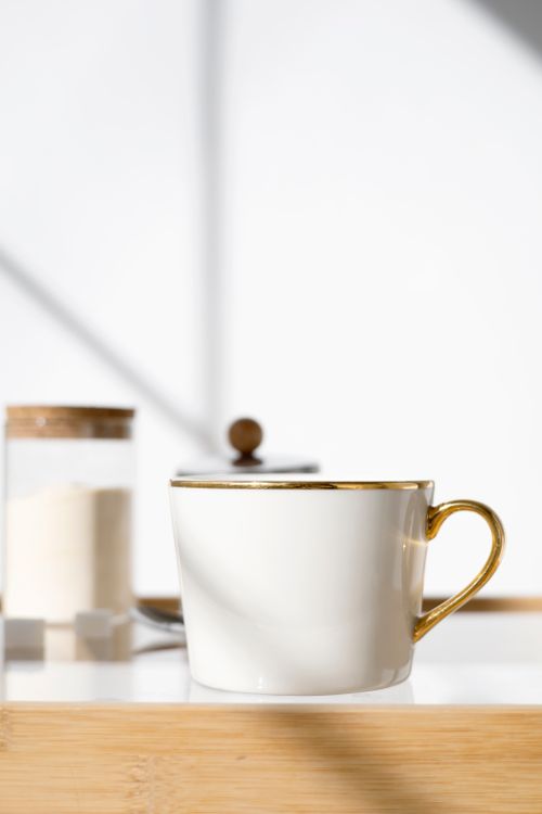 Free Stylish white ceramic teacup with gold trim on a wooden table, perfect for tea enthusiasts. Stock Photo