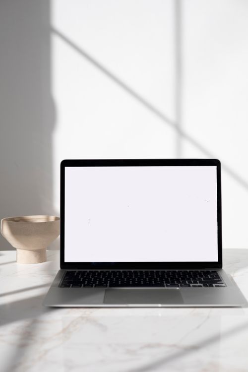 Free A sleek laptop displayed on a marble surface with natural sunlight casting shadows, perfect for tech and workspace themes. Stock Photo